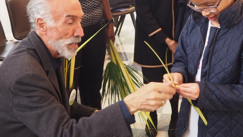 A man shows a little girl how to make a palm cross