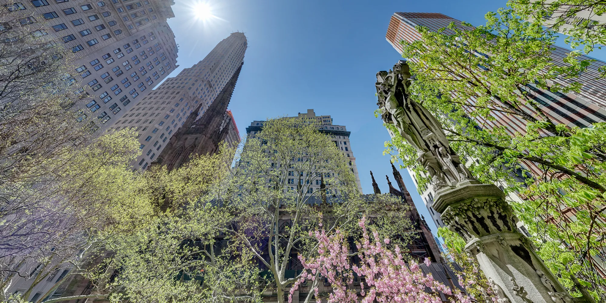 Springtime image of Trinity Church with buildings in background and Astor Cross, looking up at the sky