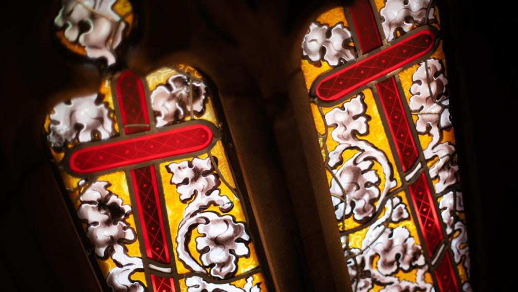 Two red crosses surrounded by a white flowering vine over a yellow background on a stained glass window in Trinity Church