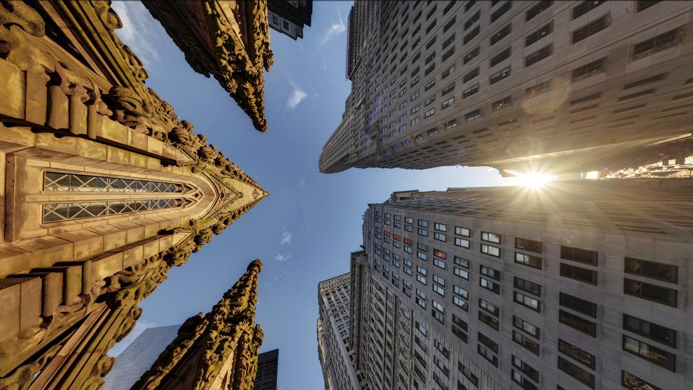 Trinity Church spire straight up with sun showing through nearby buildings.