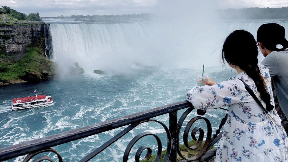 Two people look over Niagara Falls with a boat approaching the falls in the distance