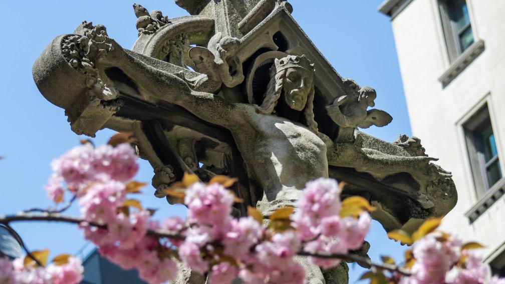 A brach of blooming pink flowers in front of the Astor cross in Trinity Churchyard