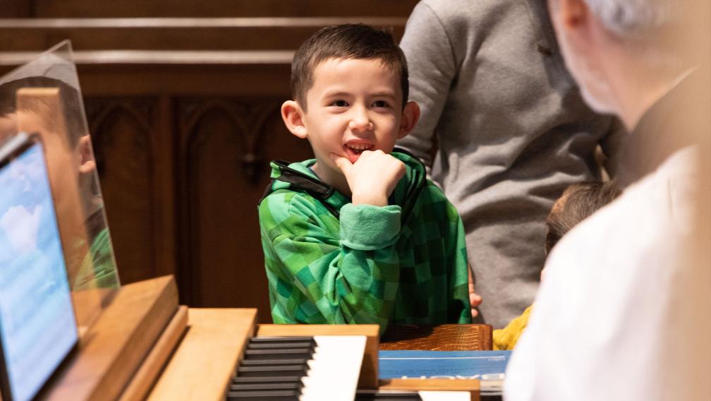 A child smiles as they perch on the edge of a keyboard in Trinity Church