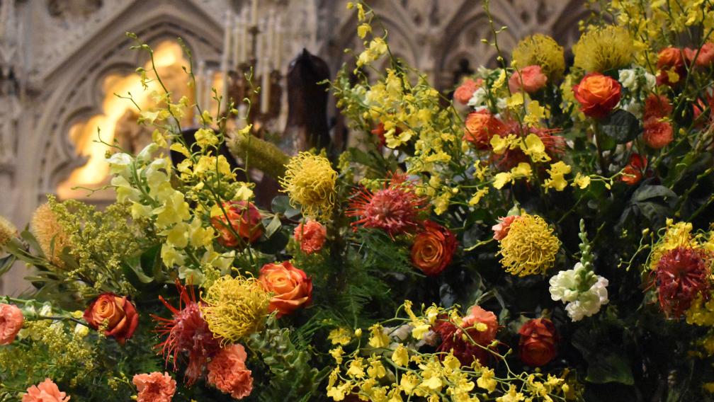An arrangement of bright yellow and orange flowers in front of the Astor reredos in Trinity Church