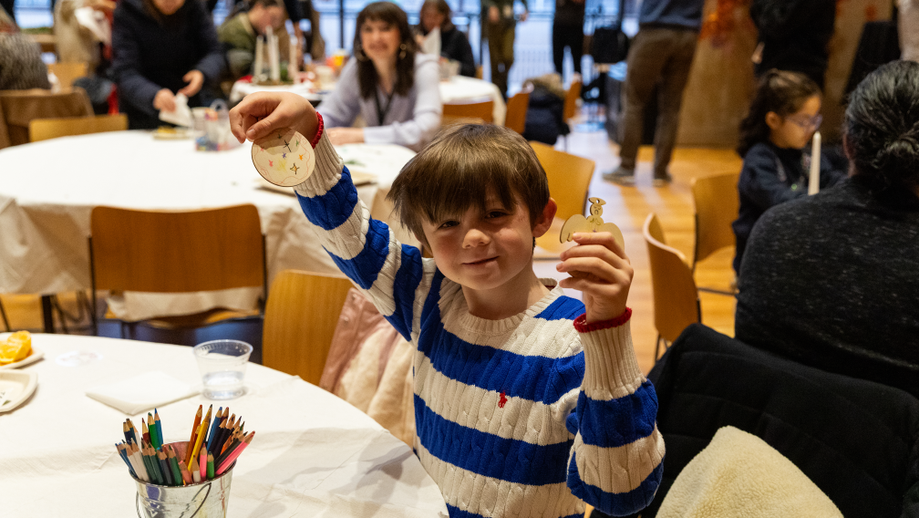 A child smiles and holds up a handmade Christmas tree ornament