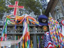 Flags, garlands, hats, a cross, and other memorial items hung on the fence surrounding St. Paul's Chapel