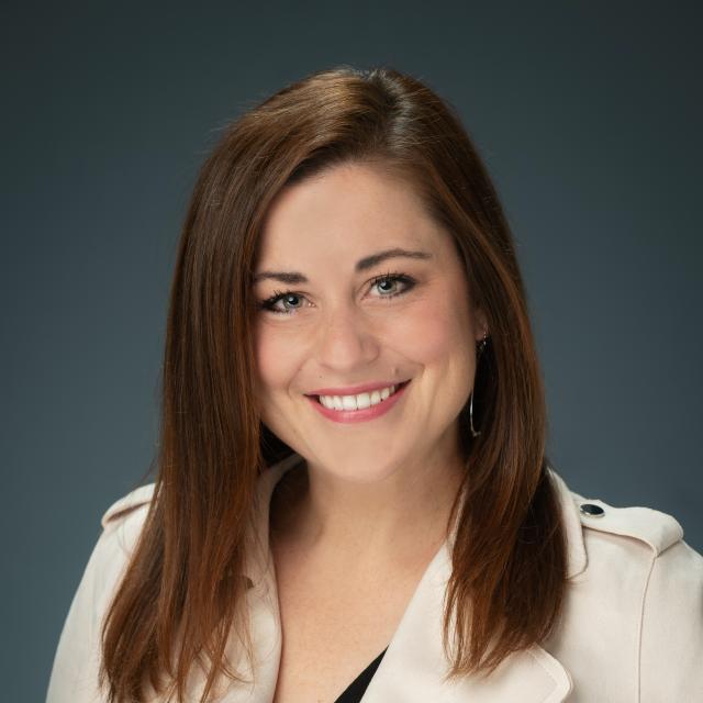 Jessica Swift smiles directly into the camera, wearing a cream motorcycle-style jacket.