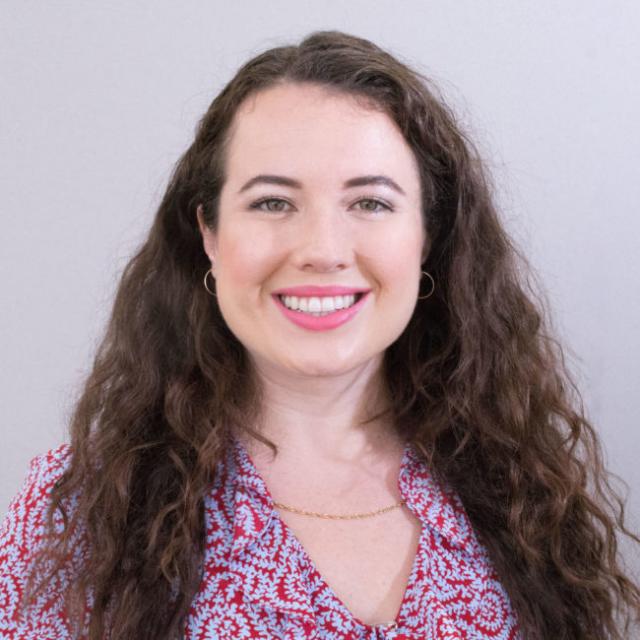 Lizzie Robins smiles at the camera, wearing a red patterned garment and hair down.