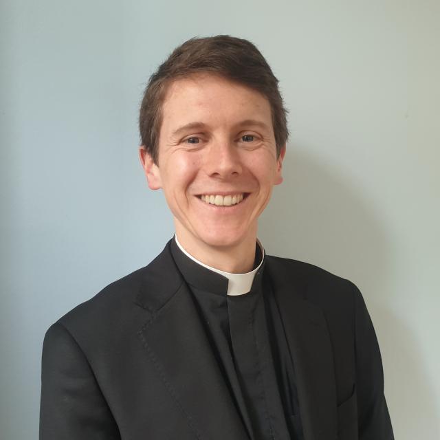 The Rev. Dr. Sam Hole smiles directly at the camera wearing clergy attire.