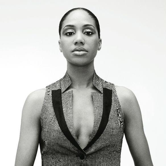 LaToya Ruby Frazier looks directly at the camera with her hair slicked back in a black-and-white photo. She wears a vest that has stylized lapels.