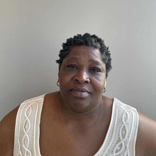 Mary Cannon softly smiles at the camera, wearing a cream cable knit scoop-neck top and small metal hoop earrings. She is a Black woman with short curly hair.