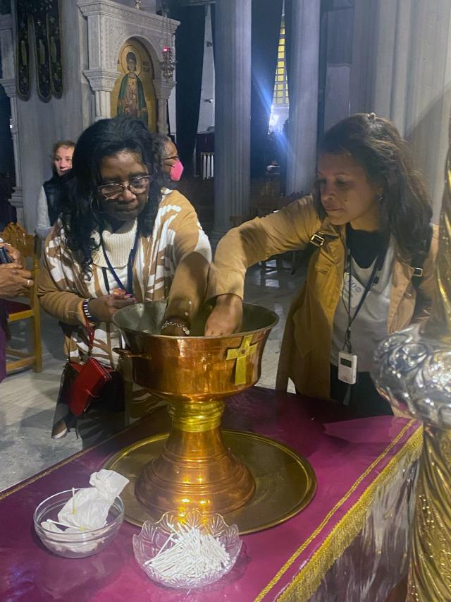 Two women dip their hands in a chalice of holy oil