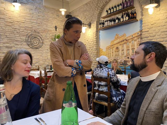 Standing woman talks to man and woman seated at table