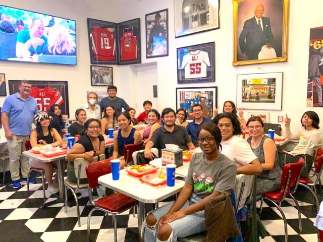 A group of smiling HYLA students and program staff sit at tables in a diner.