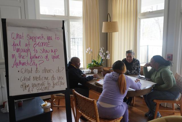 A group of four Black women sit around a table, smiling and in deep discussion at the Trinity Retreat Center.