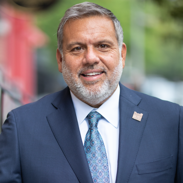 David Garza wears a suit and pin while smiling outdoors.