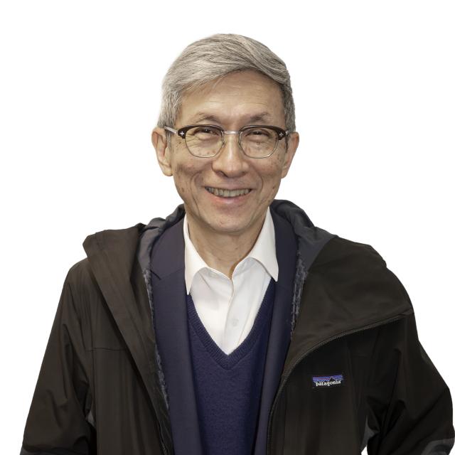 Wellington Chen smiles broadly at the camera, wearing glasses, a Patagonia jacket over a navy suit with no tie.