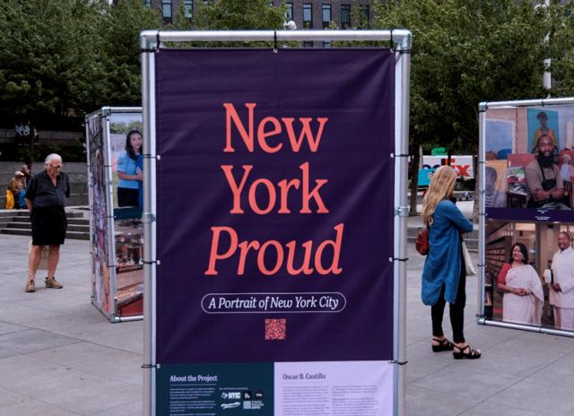 Purple poster with orange type reading "New York Proud" in an outdoor exhibition