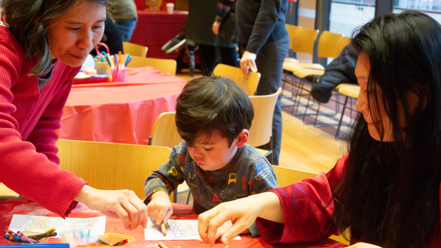 A boy colors at Trinity's Lunar New Year celebration while his mom and grandmother assist.