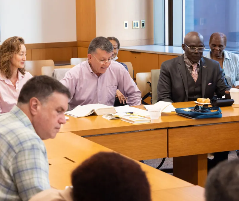 Adults meet around a wooden desk to discuss scripture.