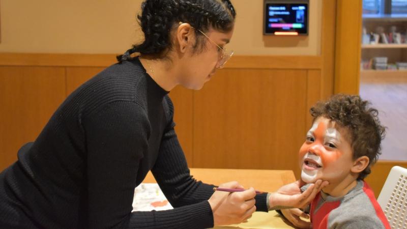 A young woman paints a boy's face 