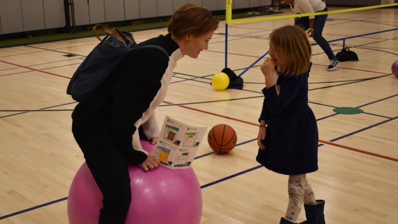 Adults and children play with an exercise ball on the basketball court.