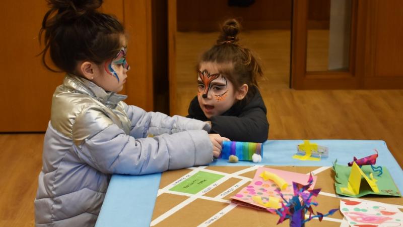 Two girls with fancifully-painted faces play at a low table.