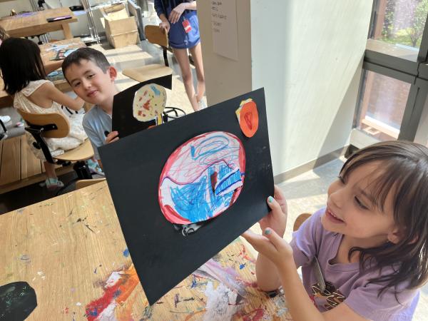 Children hold up their drawings in the Trinity Commons art studio