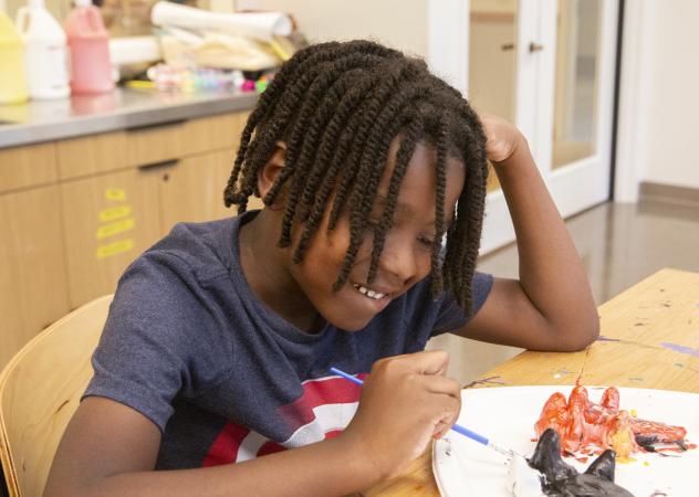 A boy paints a sculpture during the 2023 Children's Summer Program