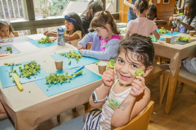 A girl holds up pieces of broccoli during a cooking class in the Trinity Commons kitchen
