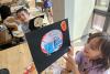 Children hold up their drawings in the Trinity Commons art studio