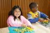 A girl smiles at the camera while chopping broccoli during the 2023 Children's Summer Program