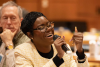 Woman speaks into a microphoto while sitting at a table in the audience of the Racial Justice Initiative Grantee Convening