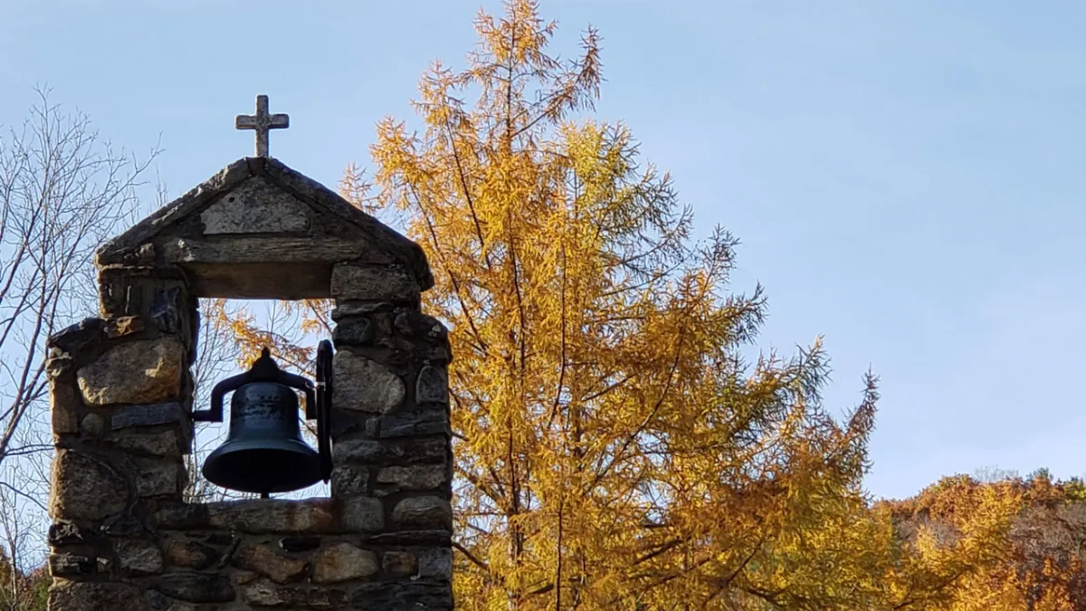 Chapel's cross and bell are framed by yellow leaves under a blue sky