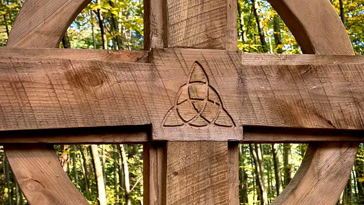A wooden cross with the green Trinity Forest behind it