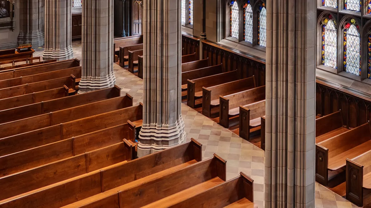 An overhead shot of wooden pews in Trinity Church lining a large wall of stained glass windows with light shining through