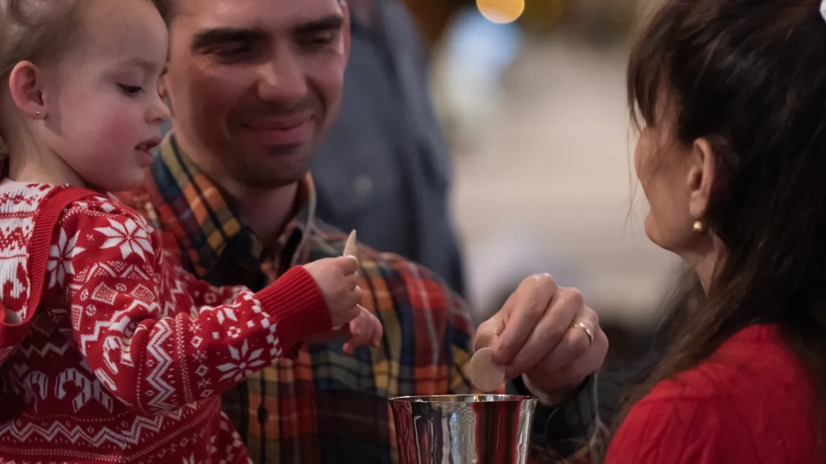 chalice bearer offers chalice to man and child during communion