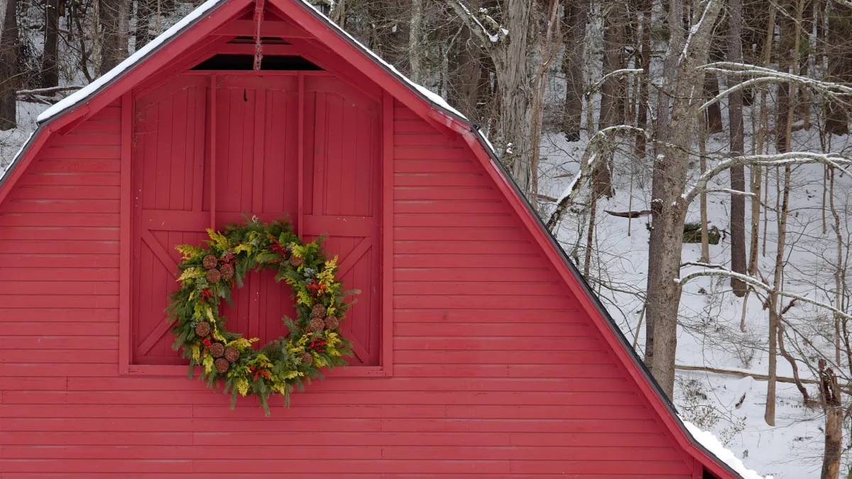 The red, wooden Retreat Center barn, decorated with a wreath, in front of snowy woods
