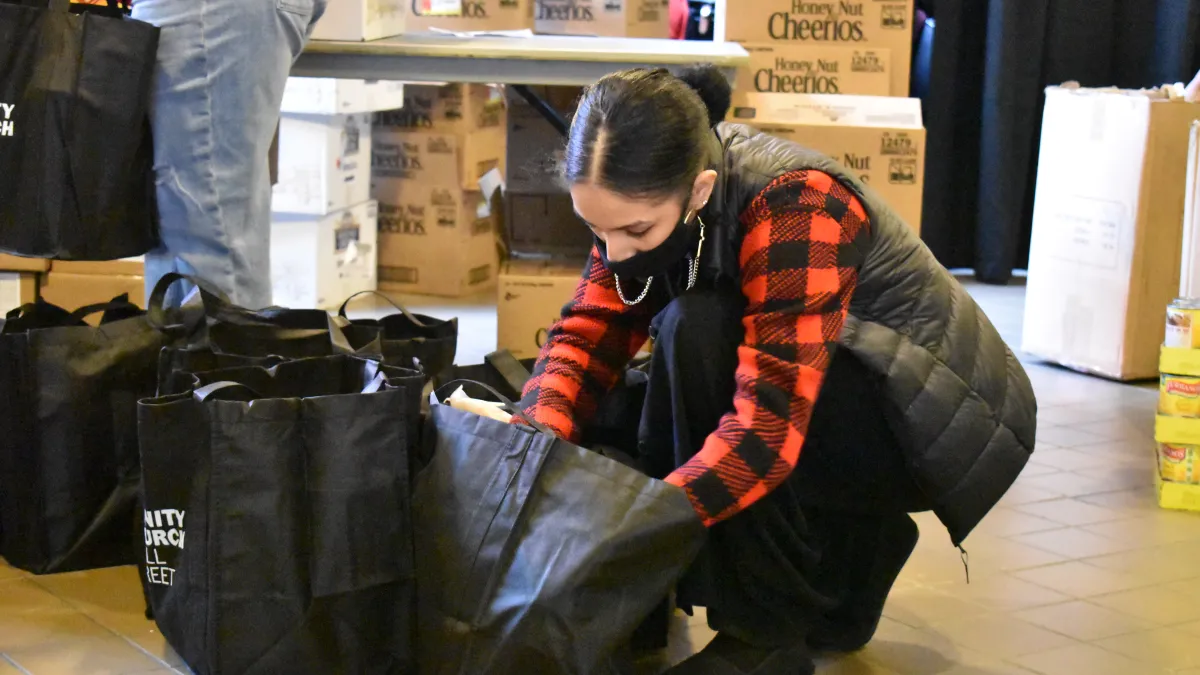 A volunteer wearing a red Buffalo check shirt and vest pack Trinity-branded tote bags with supplies.