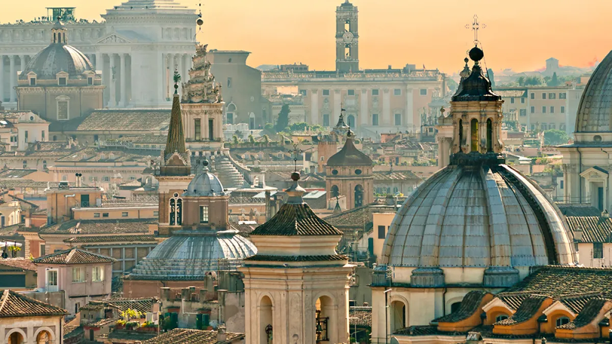 Spires and bell towers make up the skyline of Rome against a sunset
