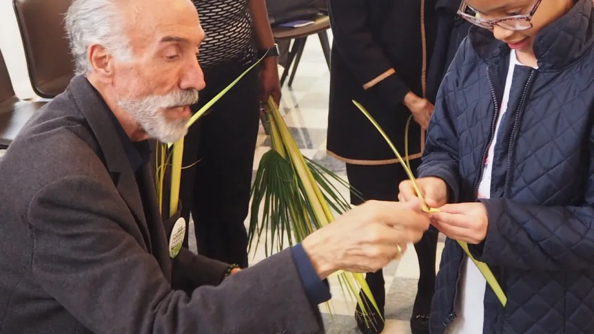 A man shows a little girl how to make a palm cross