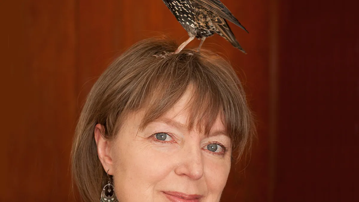 Portrait of Lyanda Lynn Haupt with a bird standing on her head.