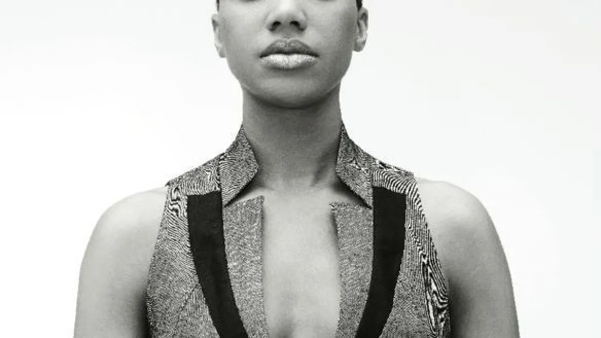 LaToya Ruby Frazier looks directly at the camera with her hair slicked back in a black-and-white photo. She wears a vest that has stylized lapels.