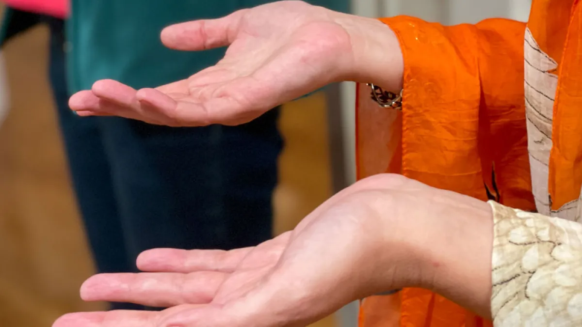 Two palms face upward, stretching out of the arms of an orange and gold robe.