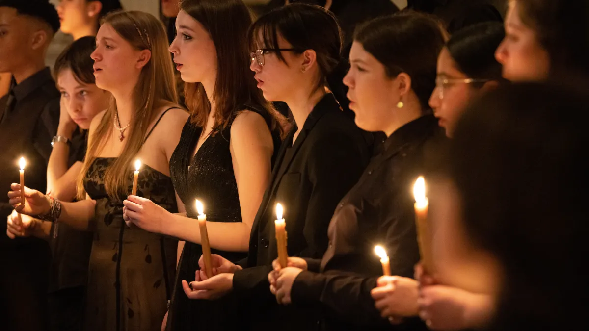 Teenagers in black clothes singing while holding candles