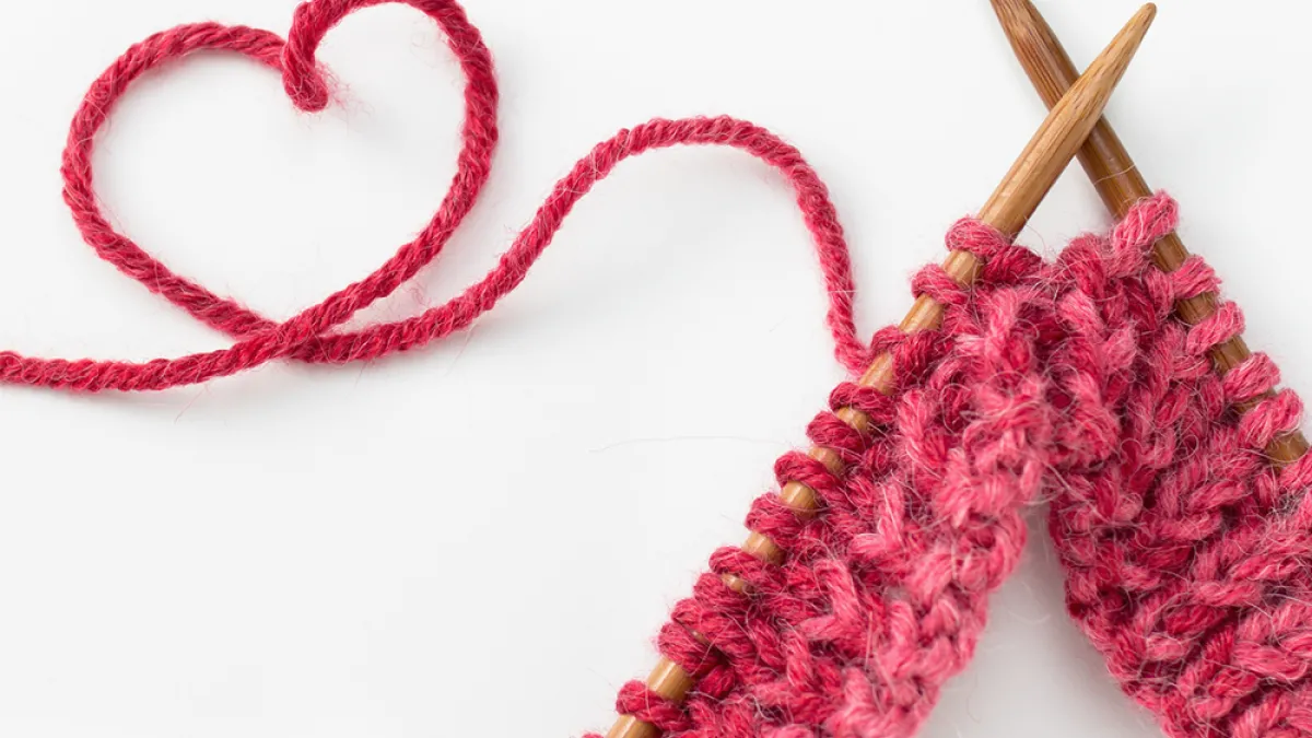 Image of knitting needles with pink yarn in the shape of a heart
