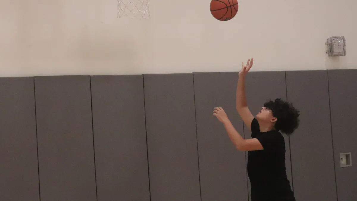 Child throws basketball to hoop in the Trinity Gym.