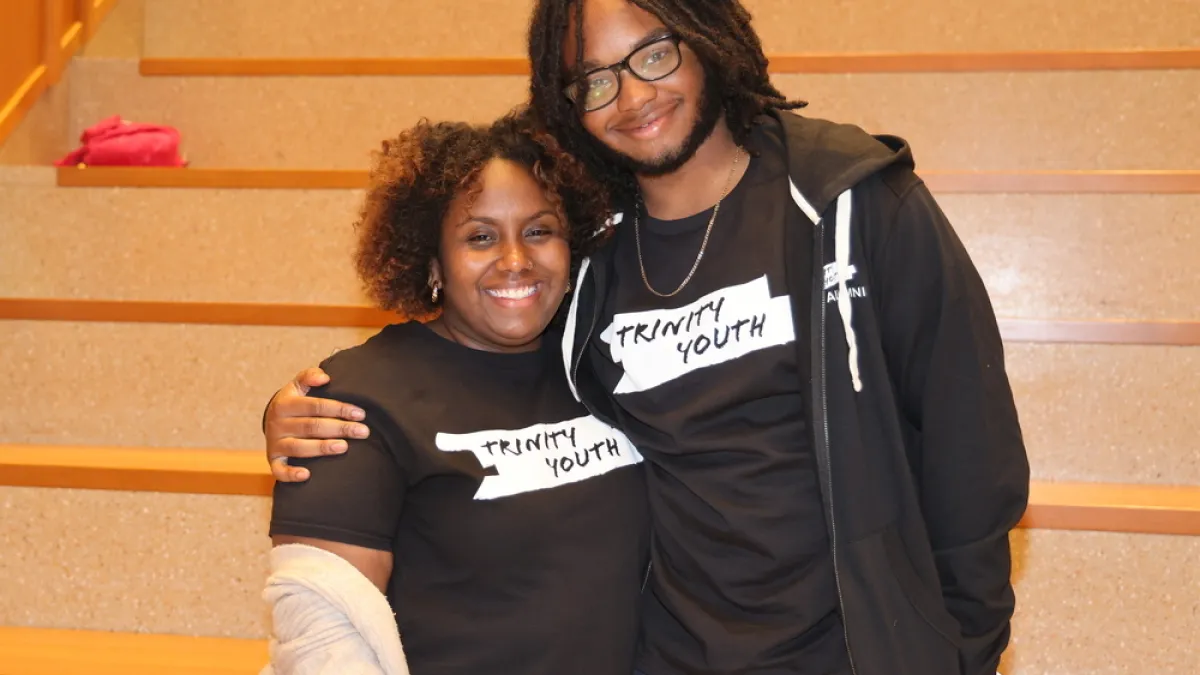 Trinity Youth staff Jayla Allen and participant smile by the staircase at the Trinity Commons lower level lobby.