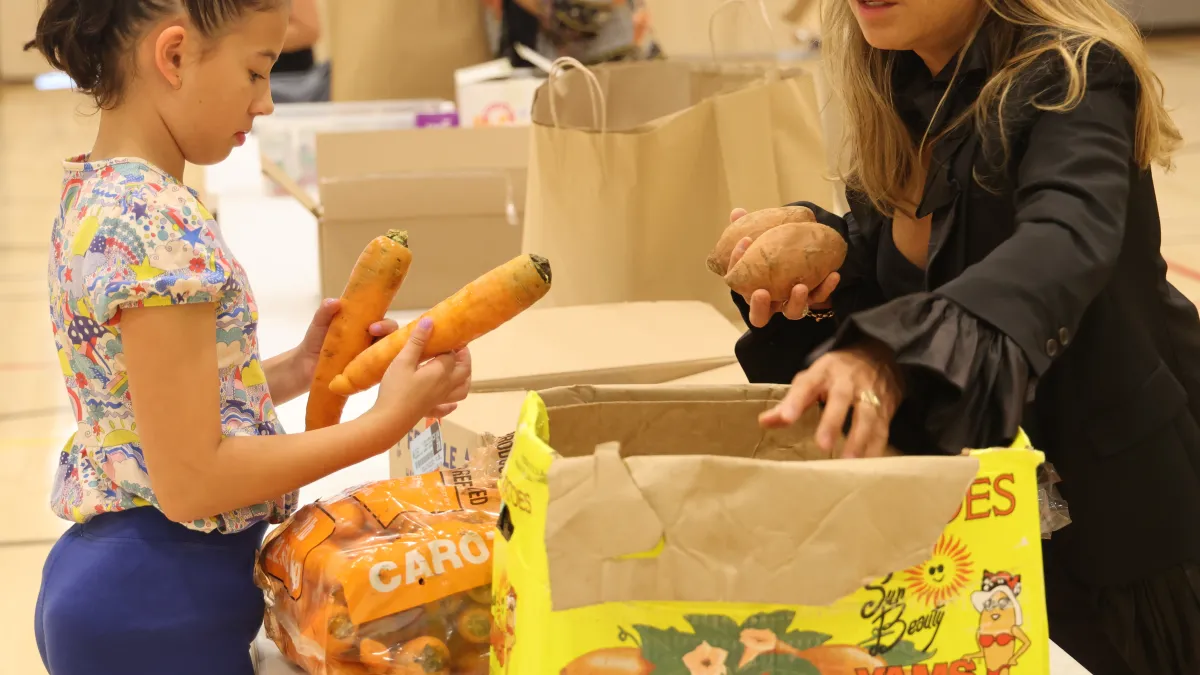 A child and adult pack carrots in a brown cardboard box.