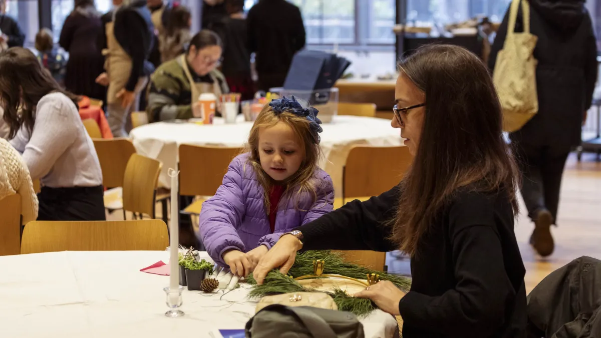 A girl makes a Christmas wreath with a lady.